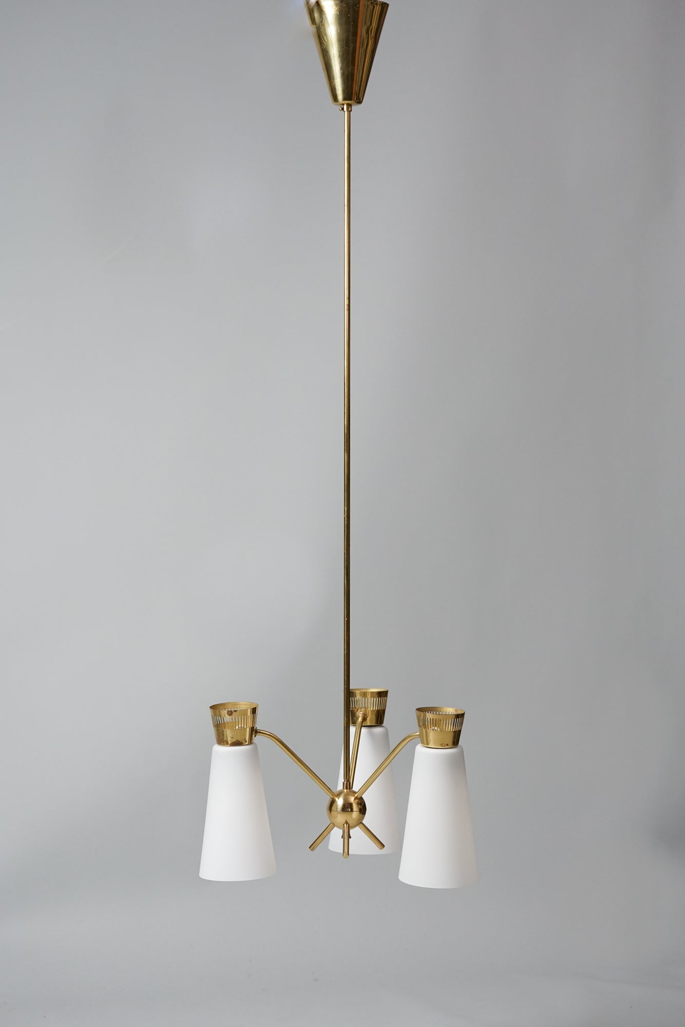 A lamp with three lights, held together by an unique ball decoration in the middle. The base is made of brass and the lamp domes of cloudy white glass.
